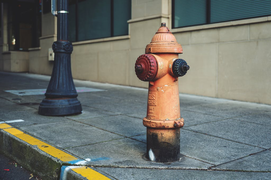 A bright orange fire hydrant on a city sidewalk against a building backdrop.