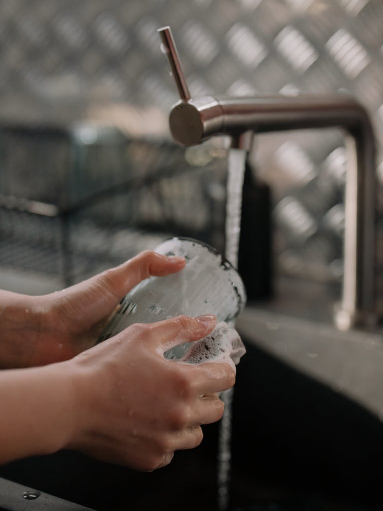 A close-up view of hands washing a glass under running water in a kitchen setting.